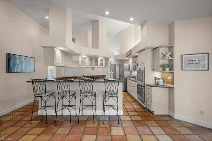 Kitchen featuring a high ceiling, a breakfast bar area, glass insert cabinets, stainless steel appliances, and light tile patterned floors