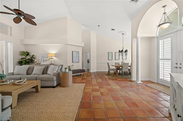 Living area with ornate columns, high vaulted ceiling, light tile patterned floors, a ceiling fan, and arched walkways