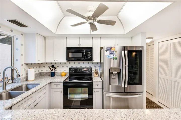 Kitchen featuring black appliances, white cabinets, light stone countertops, and ceiling fan