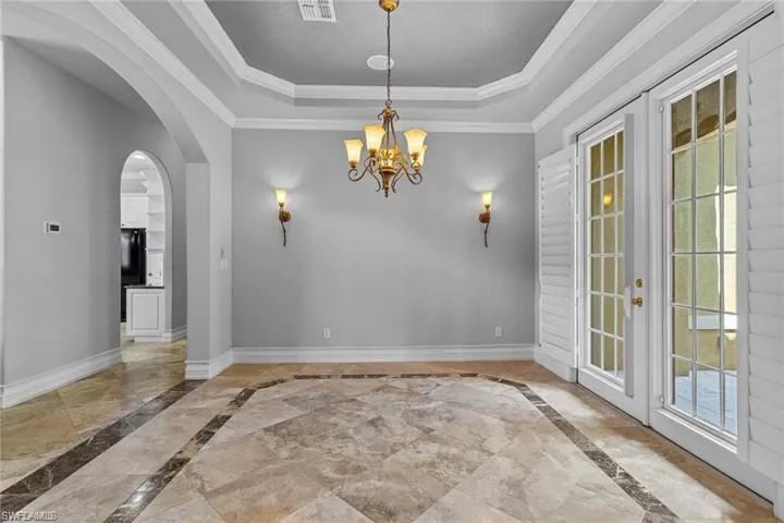Spare room featuring a tray ceiling, french doors, crown molding, and a wealth of natural light
