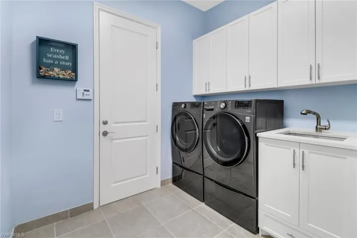 Clothes washing area featuring sink, light tile patterned floors, cabinets, and washer and clothes dryer