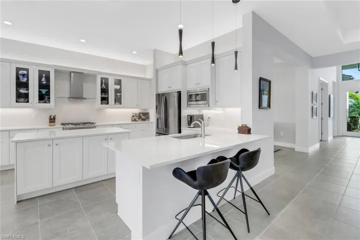Kitchen with wall chimney exhaust hood, a breakfast bar area, stainless steel appliances, sink, and decorative light fixtures