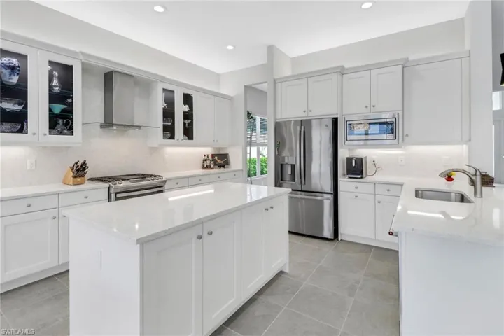 Kitchen featuring light stone counters, stainless steel appliances, wall chimney range hood, and sink