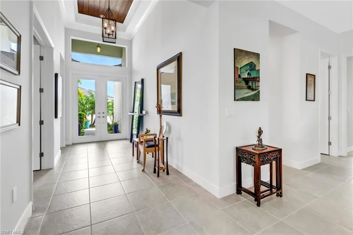 Foyer entrance with a raised ceiling, a chandelier, light tile patterned flooring, a high ceiling, and french doors
