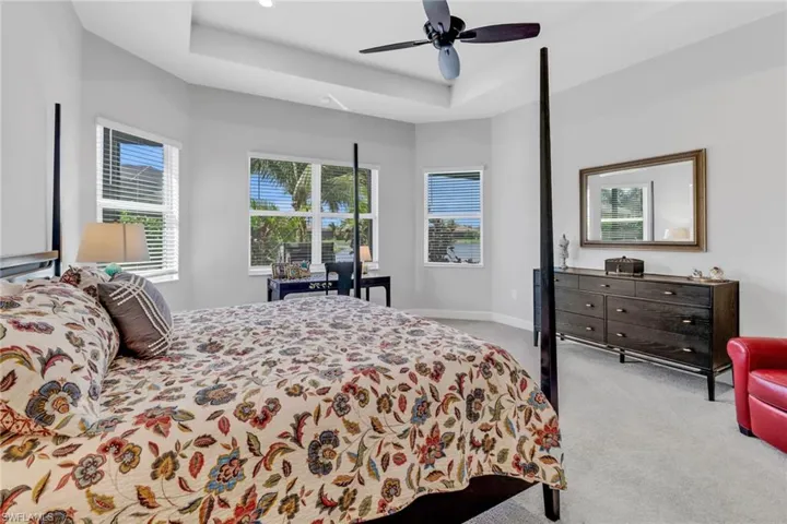 Carpeted bedroom featuring ceiling fan, a tray ceiling, and multiple windows
