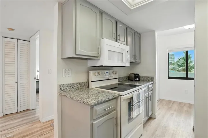 Kitchen featuring white appliances, gray cabinets, light wood finished floors, and light stone countertops