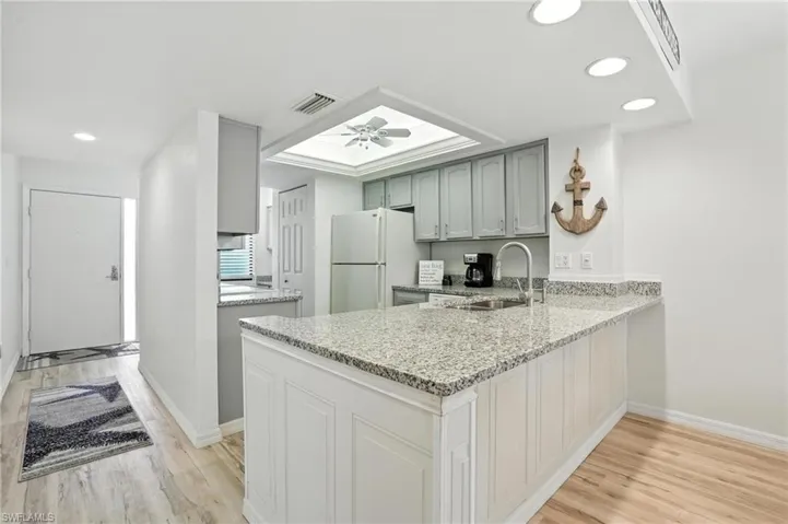Kitchen featuring freestanding refrigerator, a peninsula, light wood-type flooring, recessed lighting, and light stone counters