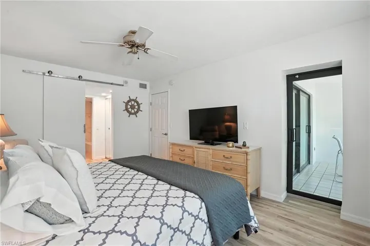 Bedroom featuring light wood finished floors, a barn door, and ceiling fan