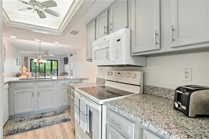 Kitchen with white appliances, a raised ceiling, a ceiling fan, light wood-style floors, and recessed lighting