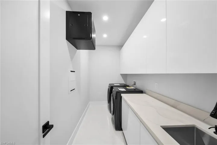 Integrated laundry area featuring white gloss cabinetry, a patterned light-toned countertop with an undermount sink, and recessed lighting