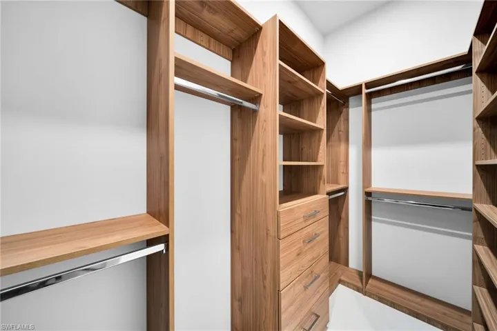 Custom built-in closet system featuring wood-finish shelving, multiple hanging rods, and integrated drawer storage with brushed nickel hardware