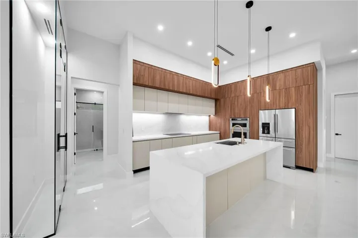 Contemporary kitchen featuring a large center island with integrated sink, stainless steel appliances, wood-finish cabinetry, and recessed lighting