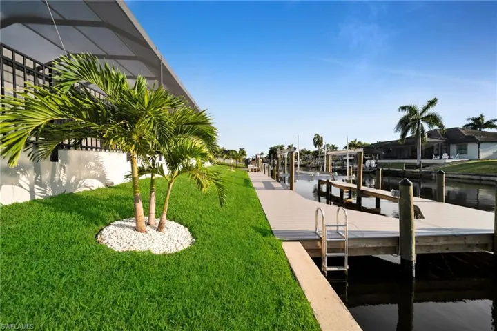 Waterfront property featuring a wood-finish dock, boat lifts, mature palm trees, and a manicured lawn