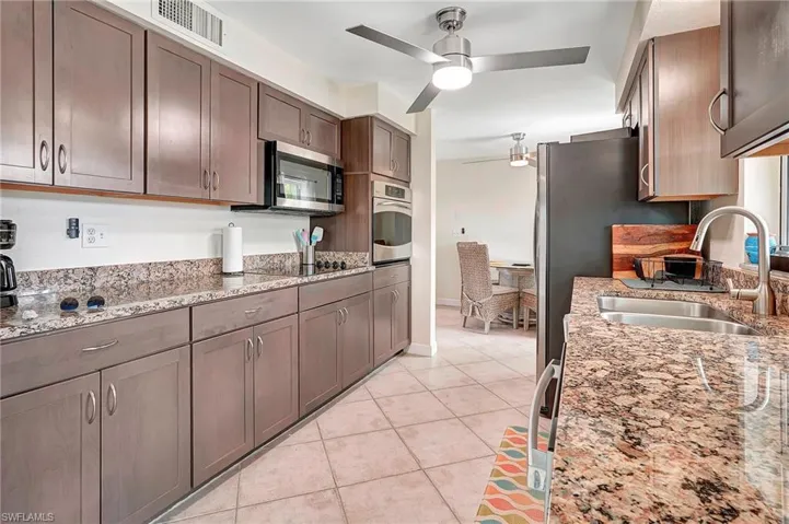 Kitchen with appliances with stainless steel finishes, sink, light stone counters, light tile patterned floors, and ceiling fan