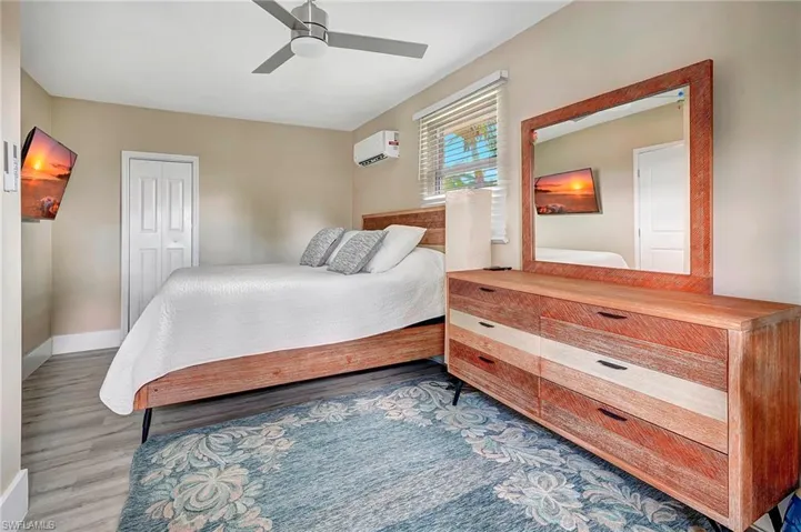 Bedroom with a wall mounted air conditioner, a closet, wood-type flooring, and ceiling fan