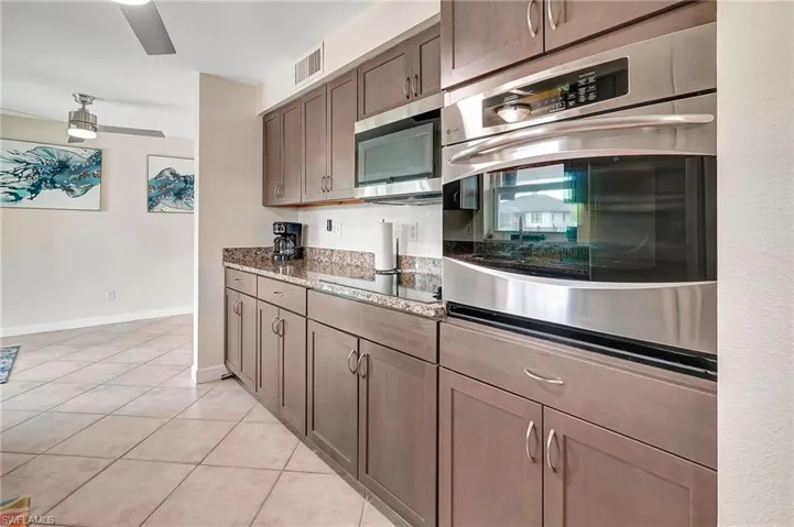 Kitchen with black electric cooktop, ceiling fan, light stone countertops, dark brown cabinetry, and light tile patterned floors