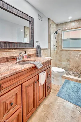 Bathroom with tiled shower, vanity, tile patterned floors, and toilet