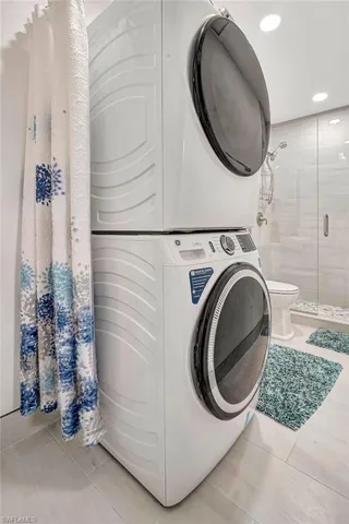Laundry area with stacked washer and dryer and light tile patterned floors