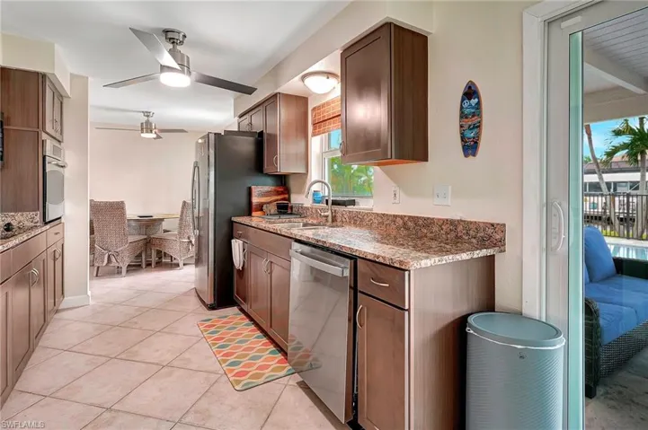 Kitchen with dark stone countertops, light tile patterned floors, ceiling fan, appliances with stainless steel finishes, and sink