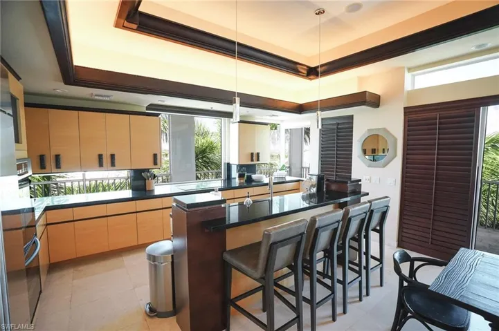 Kitchen with pendant lighting, kitchen peninsula, a tray ceiling, light brown cabinetry, and a kitchen bar