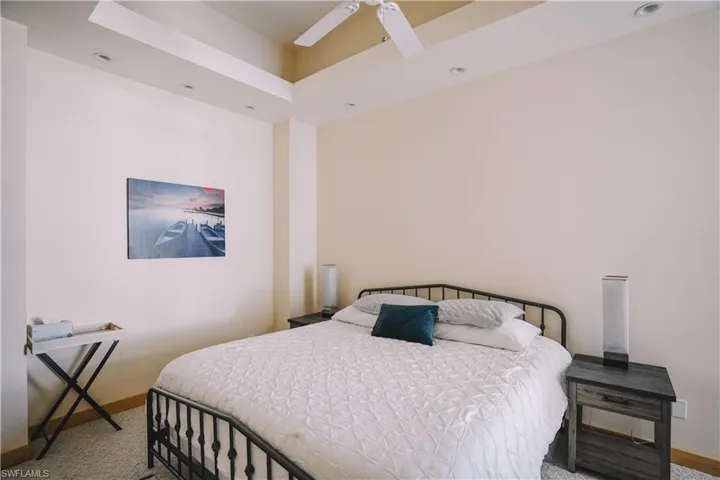 Bedroom with ceiling fan, light colored carpet, and a tray ceiling