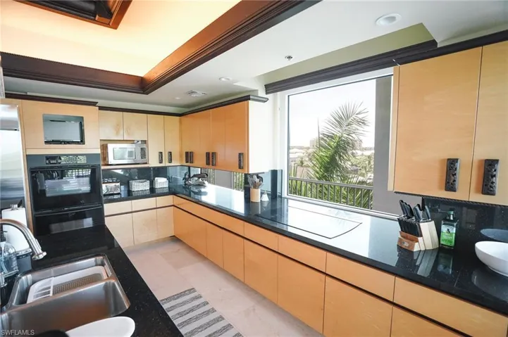 Kitchen with stainless steel appliances, dark stone countertops, light brown cabinets, and sink