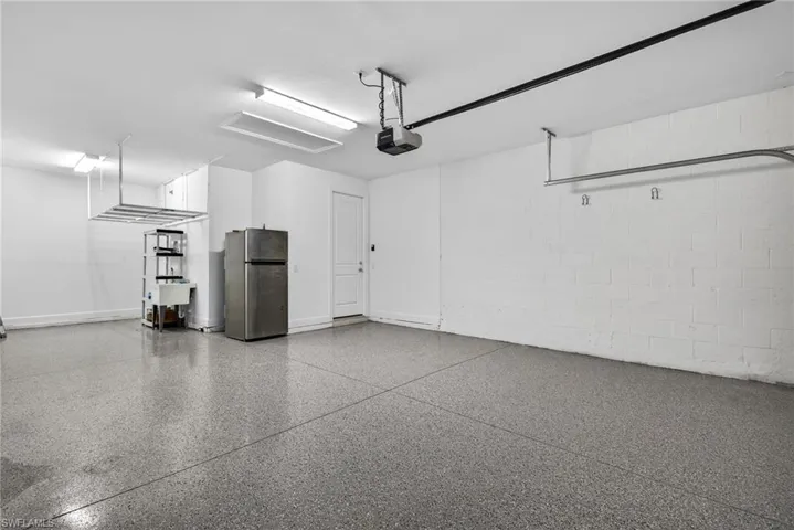 Garage with concrete block wall, freestanding refrigerator, and a garage door opener