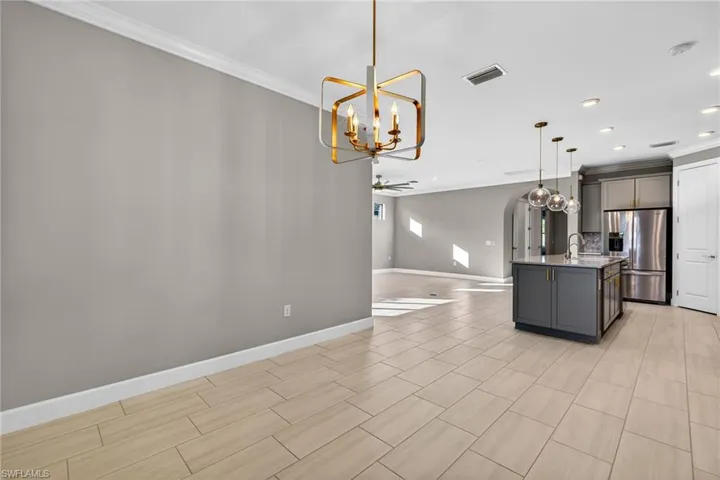 Dining room/Kitchen featuring arched walkways, open floor plan, ornamental molding, hanging light fixtures, and a kitchen island with sink