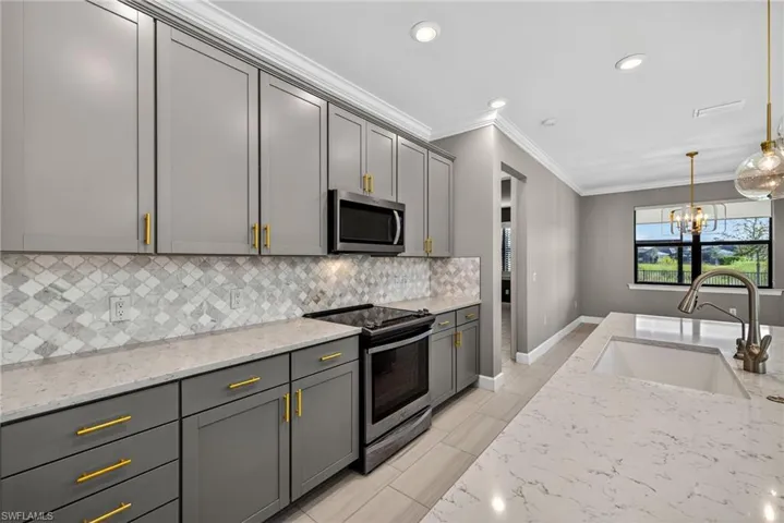 Kitchen featuring light stone counters, stainless steel appliances, pendant lighting, ornamental molding, and a chandelier