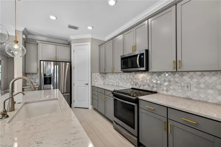 Kitchen featuring appliances with stainless steel finishes, gray cabinetry, pendant lighting, light stone counters, and crown molding