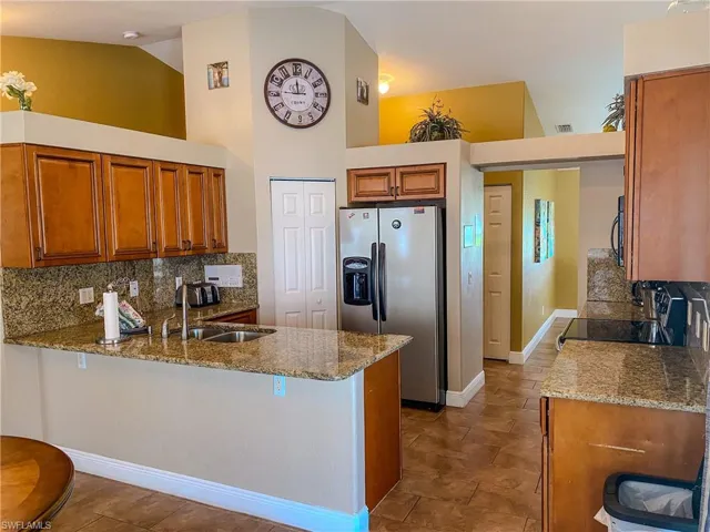 Kitchen with black range, light stone countertops, backsplash, kitchen peninsula, and stainless steel fridge with ice dispenser
