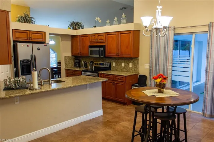 Kitchen featuring appliances with stainless steel finishes, light stone countertops, pendant lighting, a notable chandelier, and sink