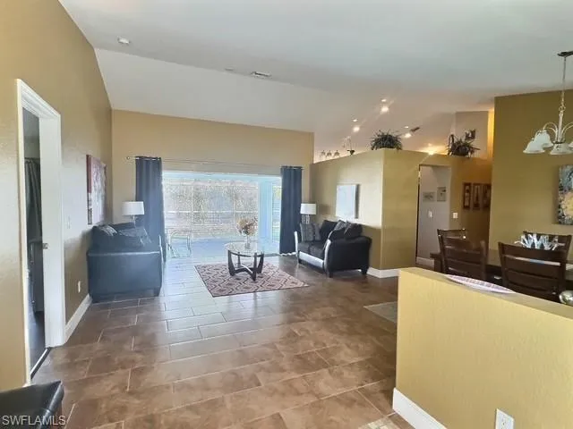 Living room with a chandelier, visible vents, baseboards, and vaulted ceiling