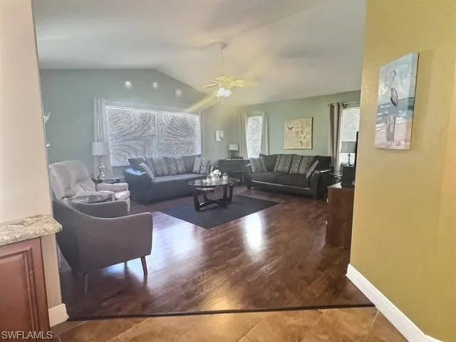 Living area featuring tile patterned flooring, vaulted ceiling, a ceiling fan, and baseboards
