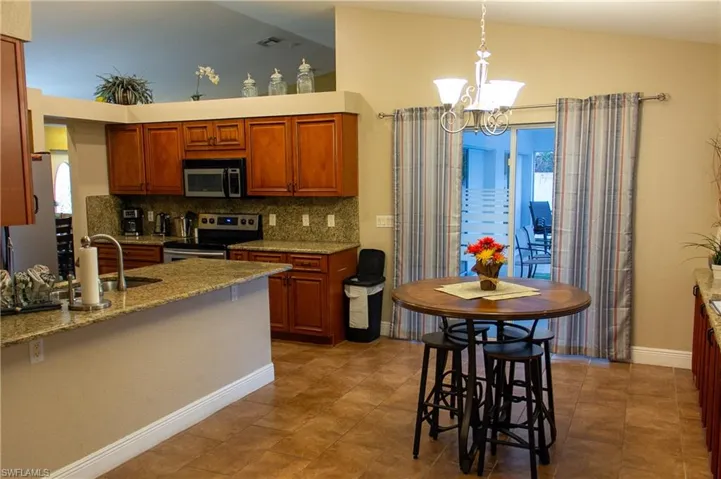 Kitchen featuring lofted ceiling, tasteful backsplash, light stone counters, appliances with stainless steel finishes, and decorative light fixtures