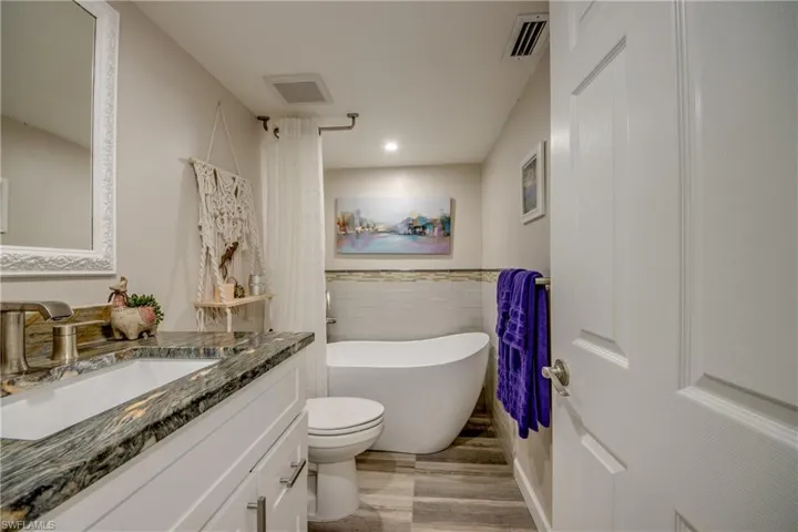 Bathroom with tile walls, hardwood / wood-style flooring, large vanity, and toilet