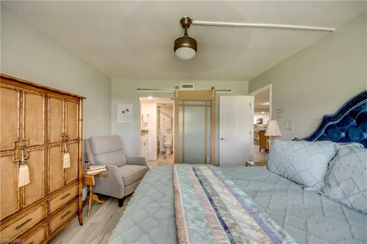 Bedroom with a barn door, light wood-type flooring, ensuite bath, and ceiling fan