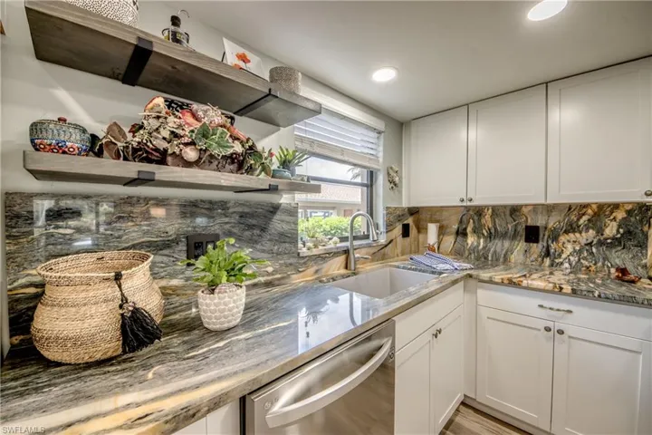 Kitchen featuring light stone countertops, dishwasher, backsplash, sink, and white cabinets