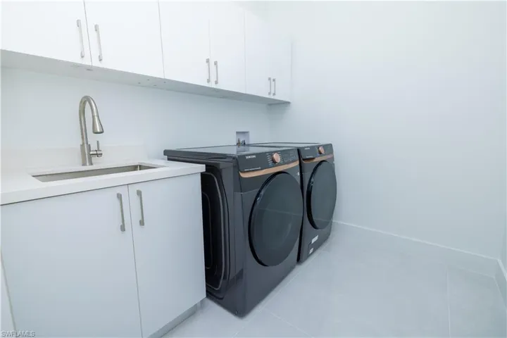 Washroom featuring washing machine and clothes dryer, light tile flooring, washer hookup, sink, and cabinets