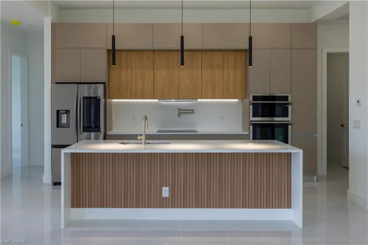 Kitchen with decorative light fixtures, light tile flooring, stainless steel appliances, a center island with sink, and sink