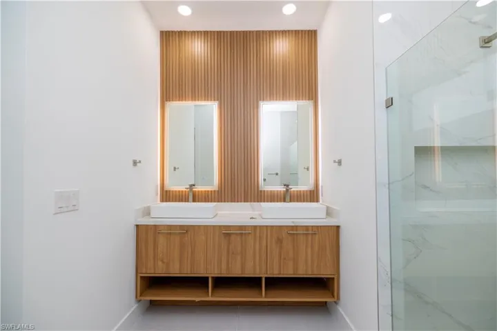 Bathroom with dual bowl vanity, tile floors, and a shower with door