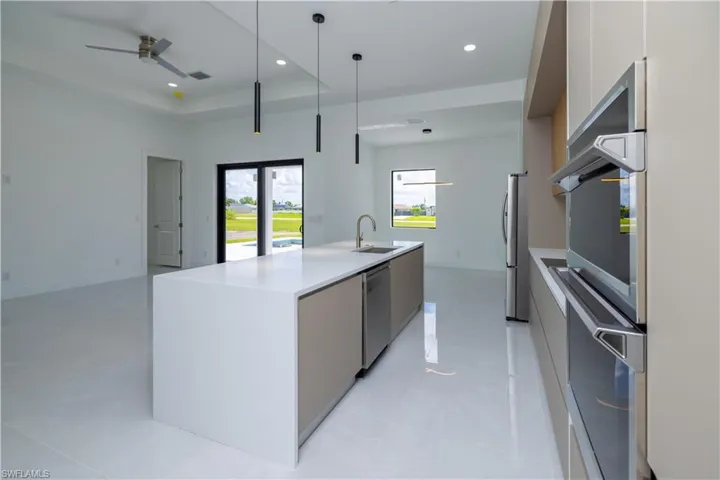 Kitchen featuring ceiling fan, an island with sink, a raised ceiling, hanging light fixtures, and sink