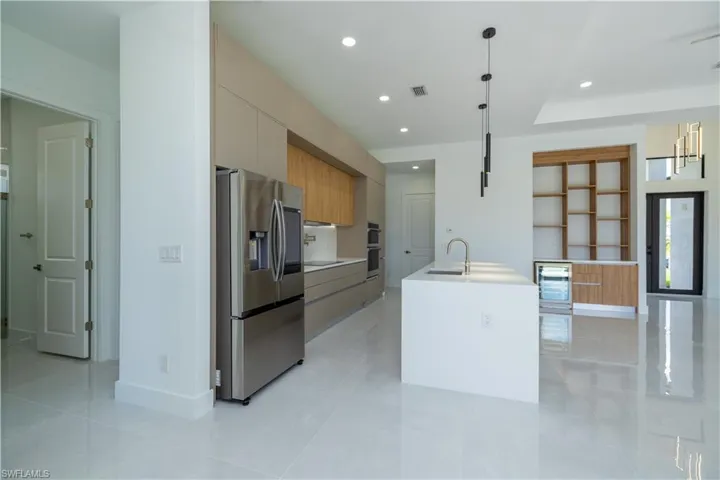 Kitchen featuring beverage cooler, an island with sink, stainless steel appliances, hanging light fixtures, and sink