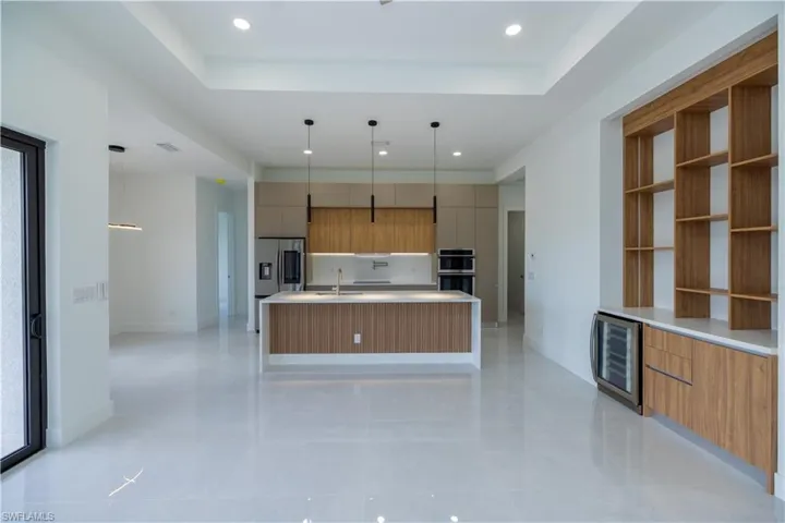 Kitchen featuring a center island with sink, a tray ceiling, beverage cooler, and appliances with stainless steel finishes