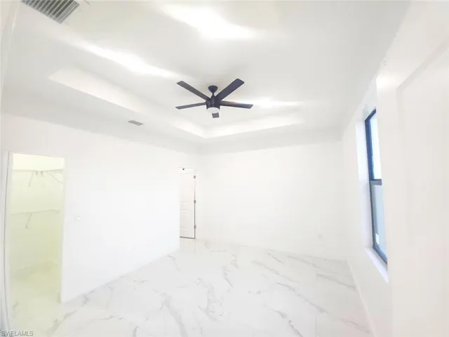 Spare room featuring a tray ceiling, a ceiling fan, and light marble finish flooring
