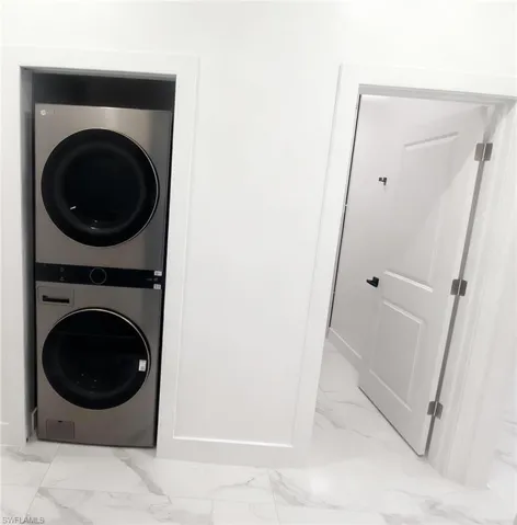 Laundry area with stacked washer / dryer and light marble finish floors