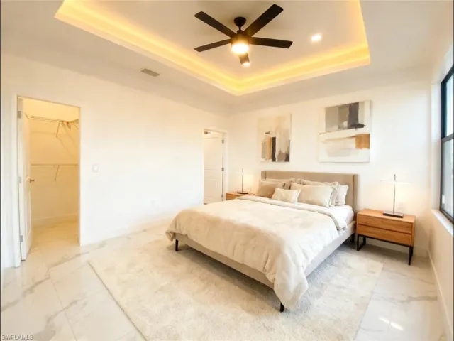 Bedroom with a tray ceiling, a ceiling fan, and light marble finish floors