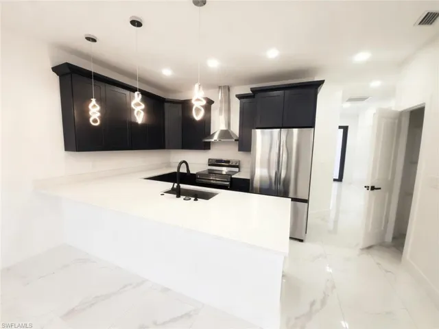 Kitchen featuring stainless steel appliances, light marble finish flooring, a peninsula, light stone countertops, and dark cabinets