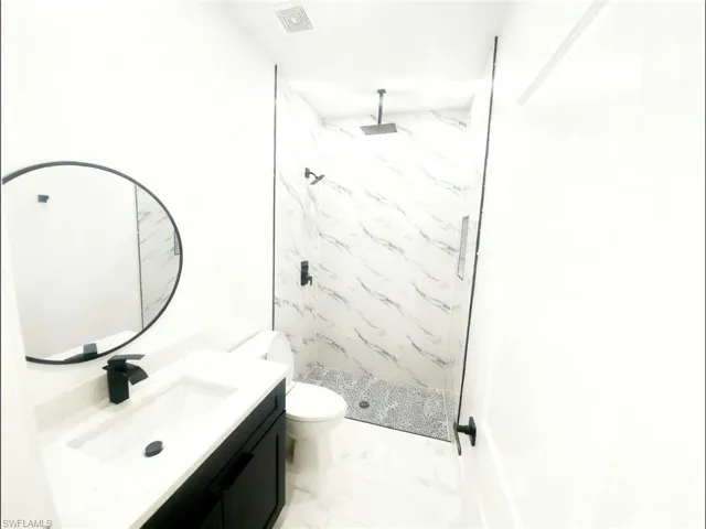 Full bath featuring vanity, a marble finish shower, and light marble finish flooring