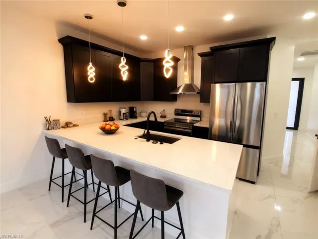 Kitchen with stainless steel appliances, exhaust hood, a kitchen breakfast bar, a peninsula, and light marble finish floors